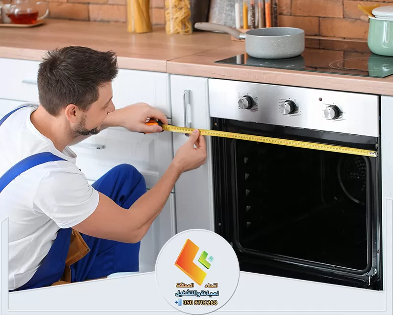 تغيير قطع غيار تالفة لافران الغاز بالرياض رجل في ملابس عمل يصلح فرن غاز مع قطع غيار جديدة بالرياض
