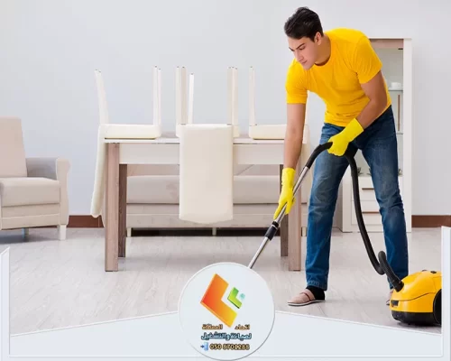 تنظيف أرضية المنزل بالمكنسة الكهربائية داخل غرفة مرتبة ومضيئة.