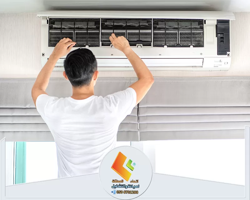 فك وتركيب مكيفات بالرياض 0578673748 اتحاد المملكة شخص يقوم بتنظيف وفك وتركيب مكيفات بالرياض مركب على الحائط، حيث يفتح الجزء الأمامي لإزالة الفلاتر.