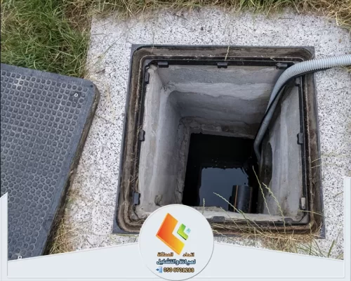 فتحة صرف أرضية مفتوحة يظهر بداخلها تجمع مياه، مع خرطوم ممتد إلى داخل المجرى لتنفيذ أعمال التنظيف.