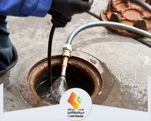 عامل يستخدم خرطوم ضغط المياه لتسليك وتنظيف فتحة صرف أرضية.
